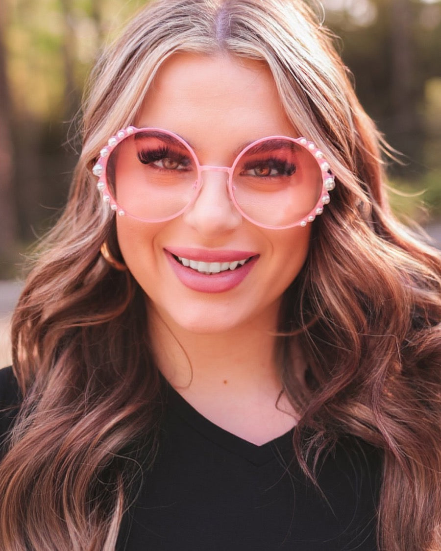 pink round sunglasses with scalloped edges and mixed-sized pearl trim around the frames, UV protection, and brand name detail (on both the temple and the complimentary black pouch)