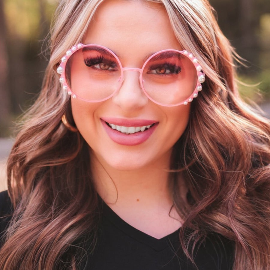 pink round sunglasses with scalloped edges and mixed-sized pearl trim around the frames, UV protection, and brand name detail (on both the temple and the complimentary black pouch)