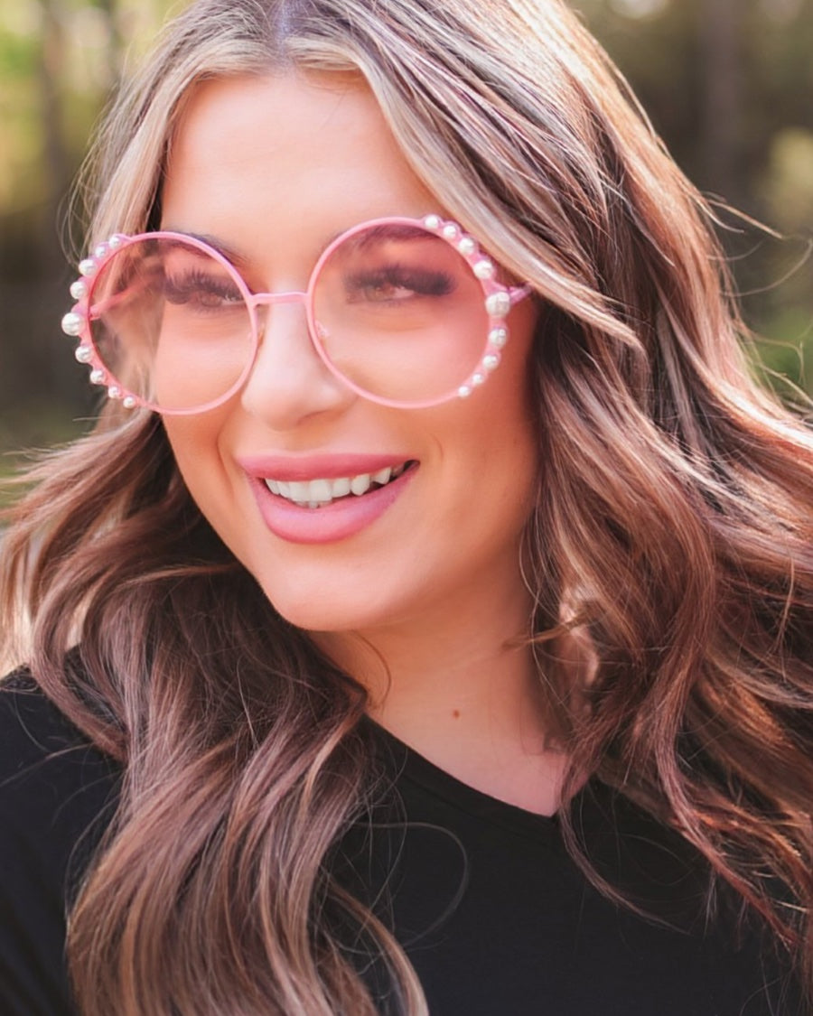 pink round sunglasses with scalloped edges and mixed-sized pearl trim around the frames, UV protection, and brand name detail (on both the temple and the complimentary black pouch)