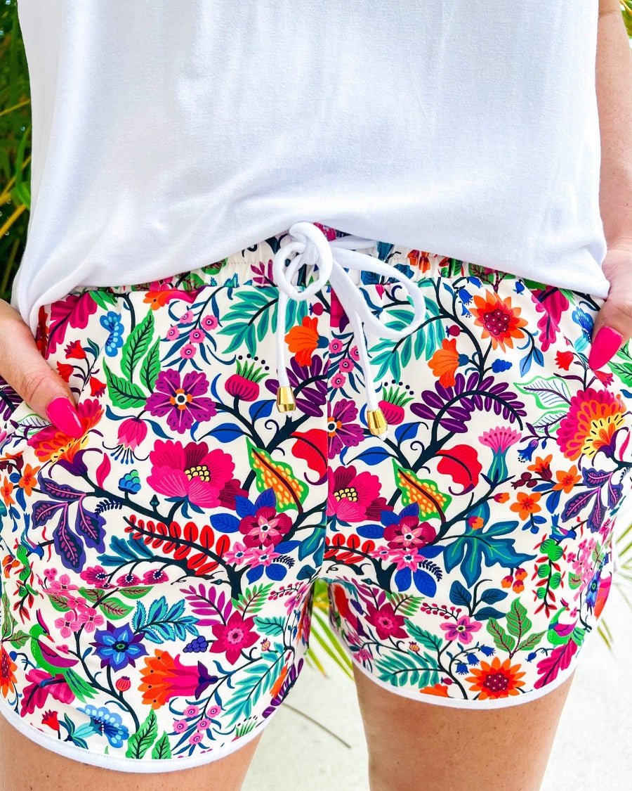 mid-rise relaxed fit activewear shorts with side pockets and a tie waist drawstring with gold bead accents, designed on a vibrant floral pattern print fabric, matching base, and matching trim