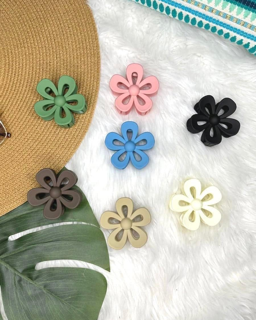 Colorful flower-shaped hair accessories on a textured white surface with a straw hat and green leaf.