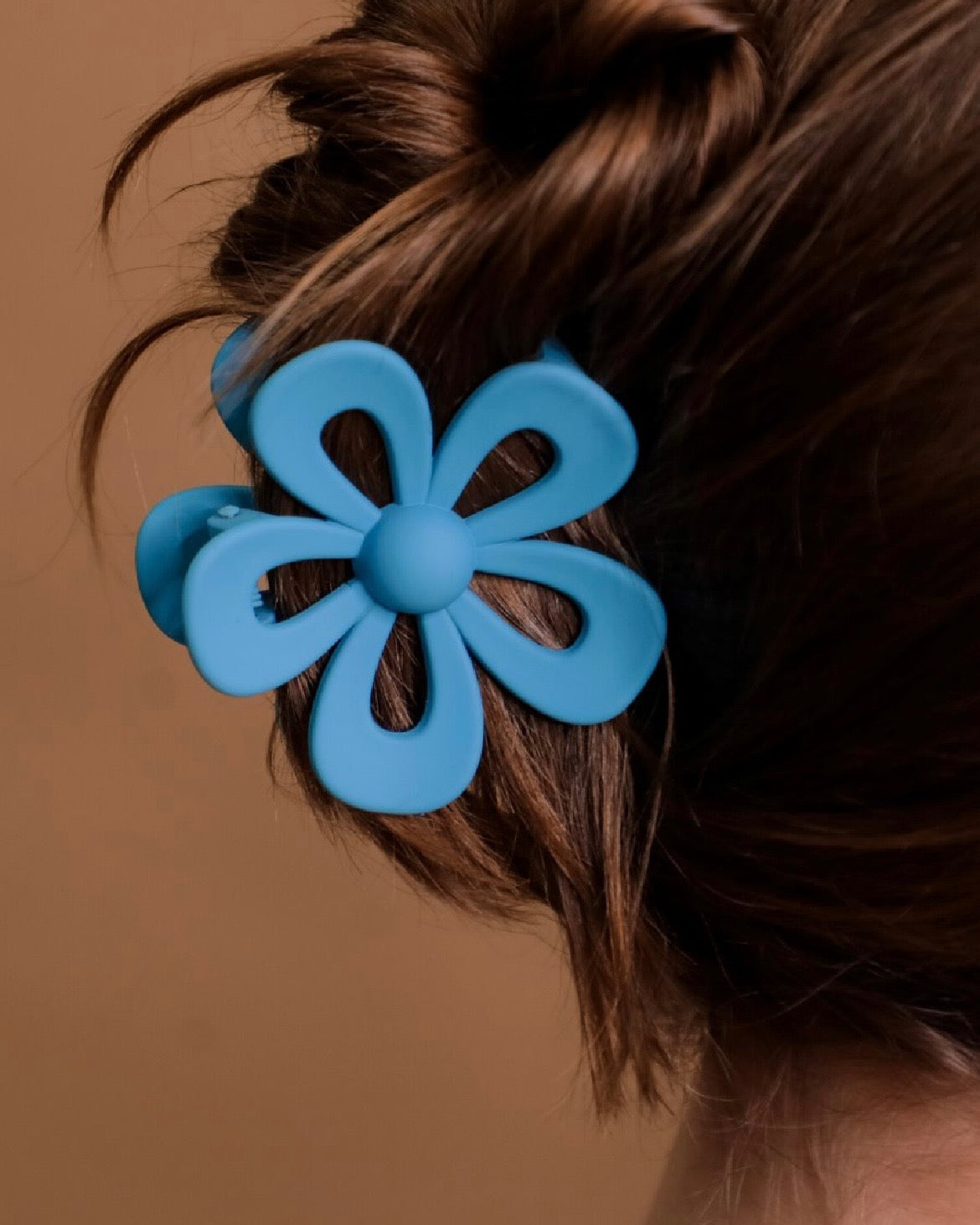 Blue flower-shaped hair clip on a person's hair against a brown background