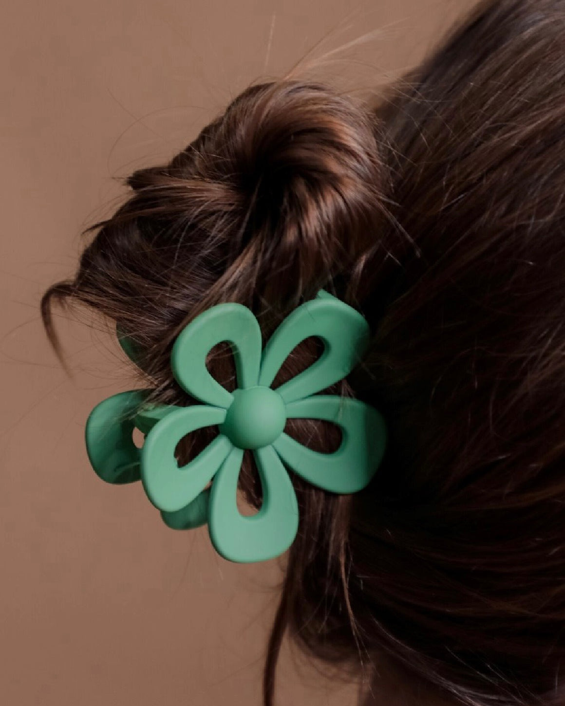 Green flower-shaped hair clip on a person's hair against a brown background