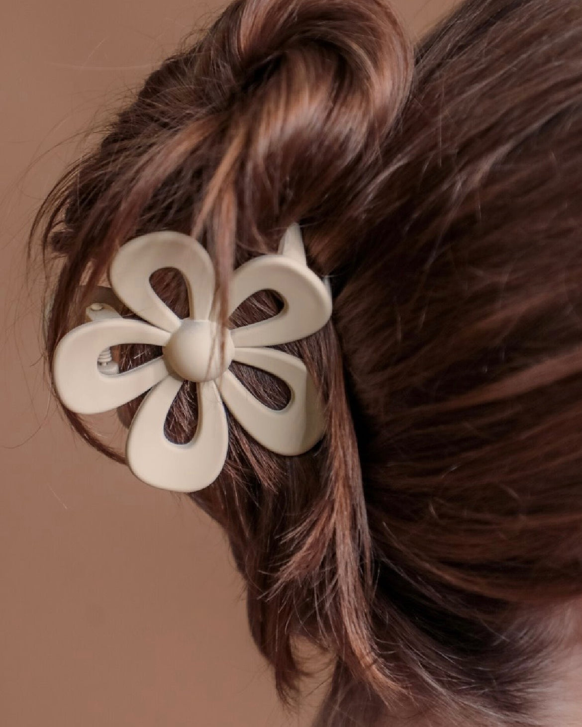 Tan flower-shaped hair clip on a person's hair against a brown background