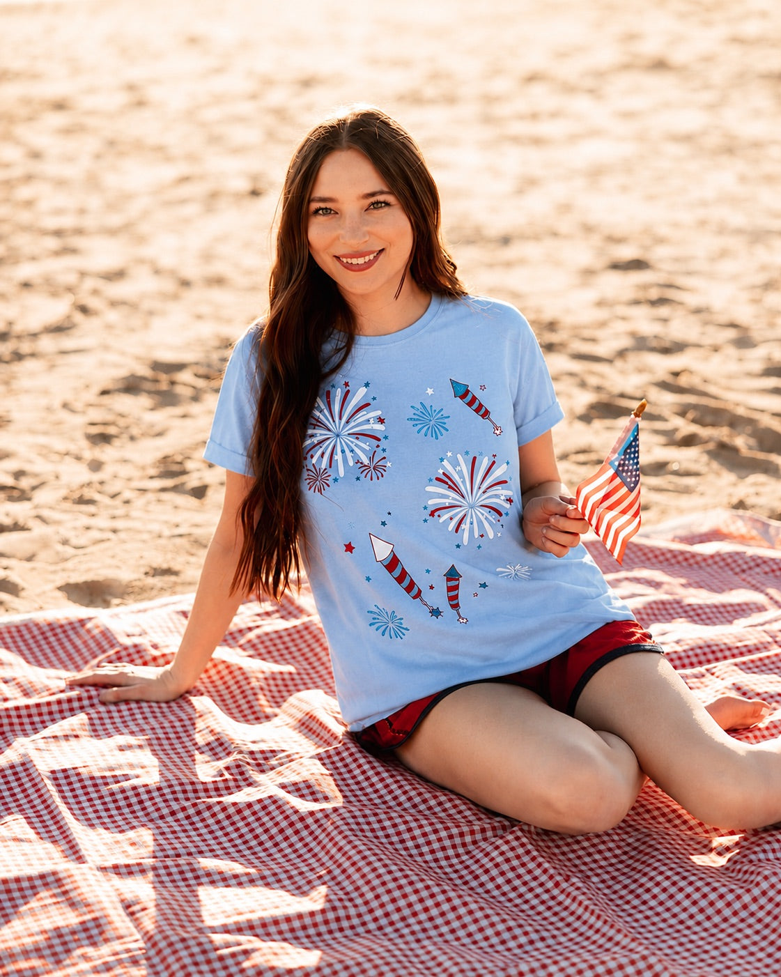 a relaxed blue crew neck tee with a screenprinted fireworks design (rockets, bursts, and starry details), short sleeves, standard t-shirt length, unlined construction, and soft cotton with light stretch