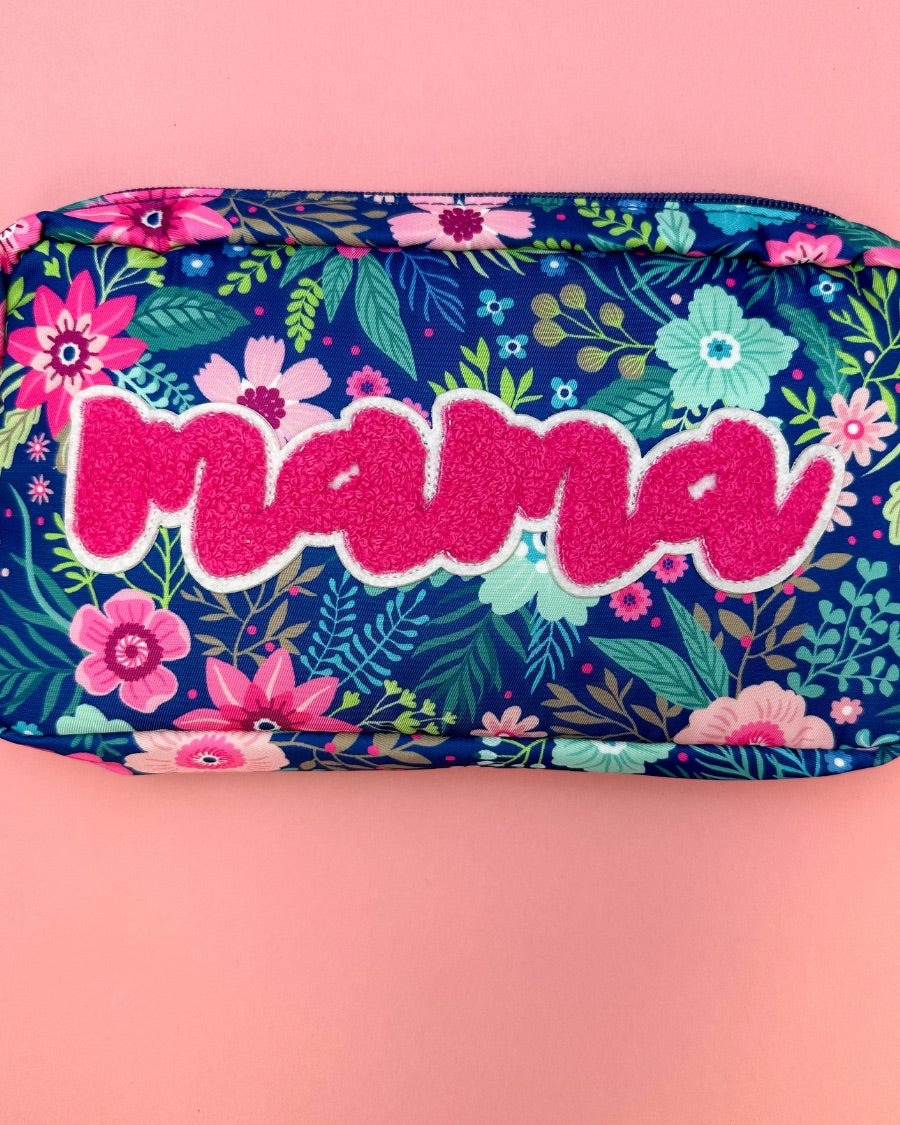 a lightweight spacious travel bag with a unique navy floral pattern (aqua, green, pink, and teal), a bold hot pink chenille 'mama' patch with white trim, and a zipper closer