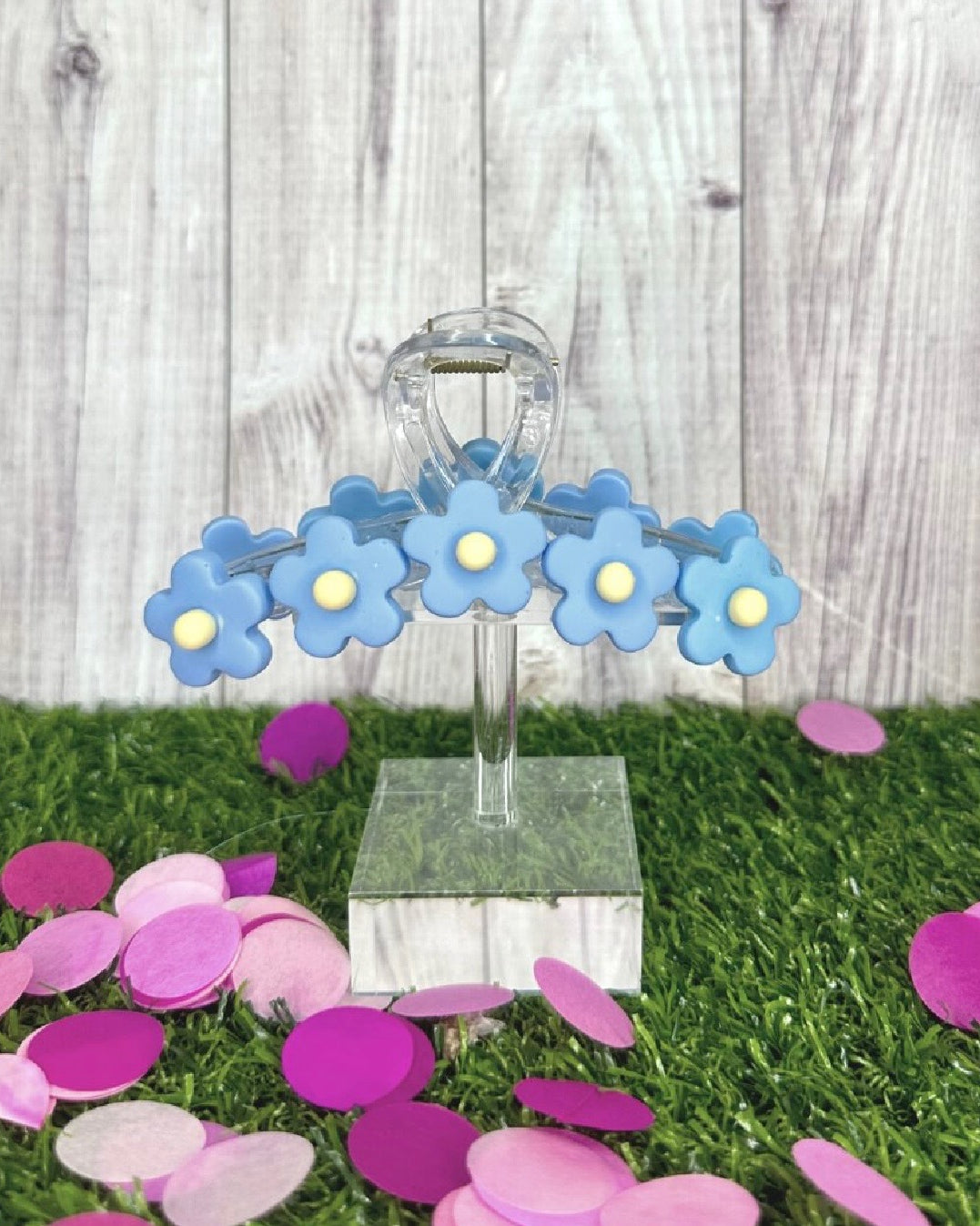 Decorative stand with blue flower-shaped objects on a grassy surface with pink confetti.