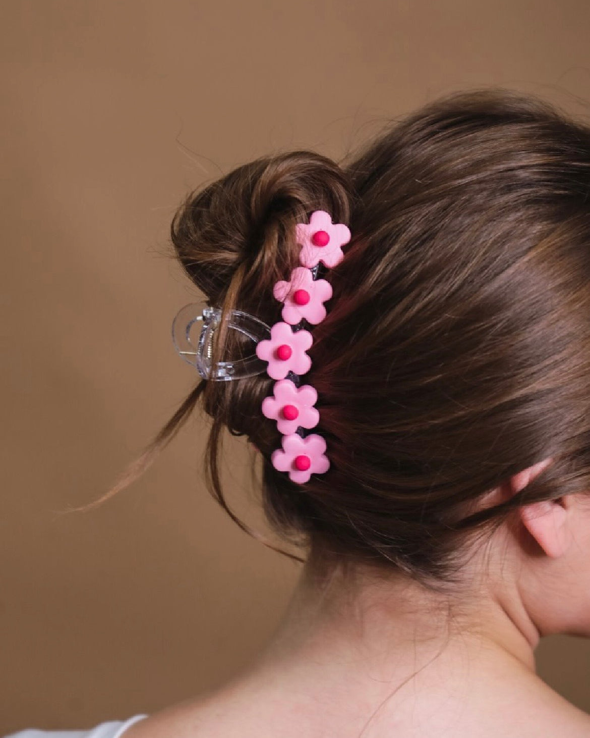 Pink flower-shaped hair clip in a bun against a neutral background