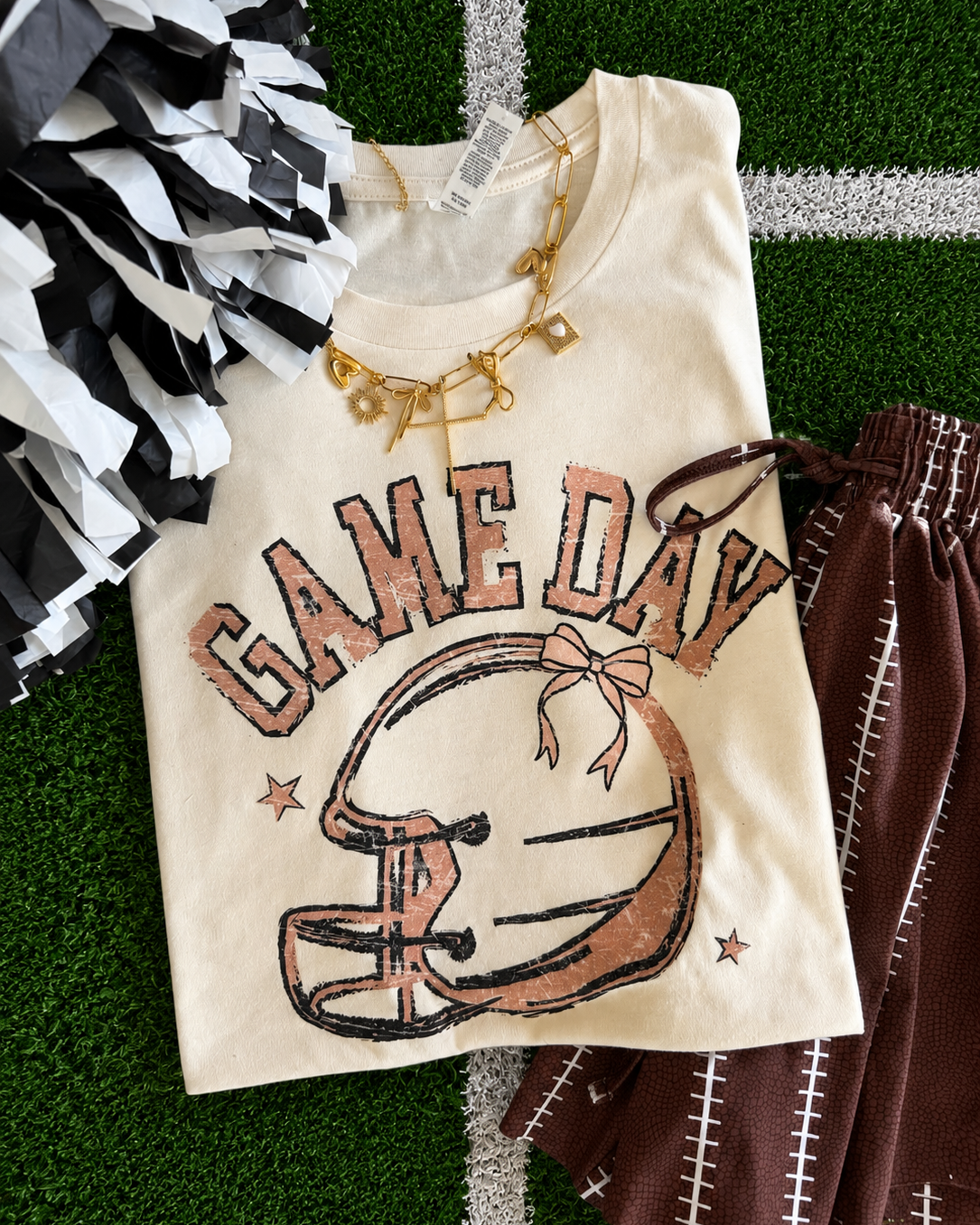 a heather natural Bella+Canvas unisex soft tee with a DTF-printed vintage-inspired football helmet, bow accent, arched 'GAME DAY' varsity lettering, star details, crew neckline, short sleeves, and a relaxed fit in both youth and adult sizing