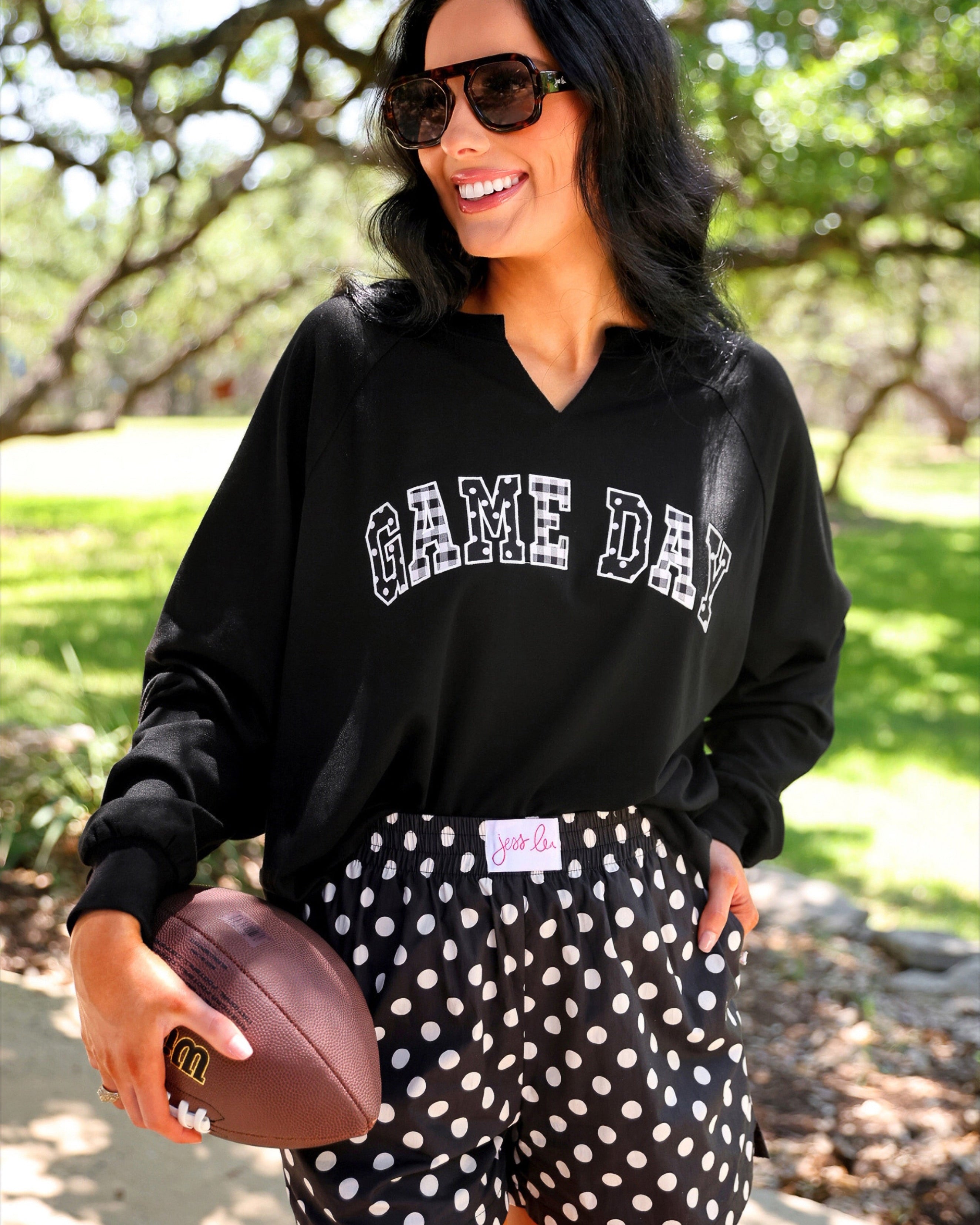 a relaxed black French terry pullover with a V-neckline, mixed polka dot and gingham 'GAME DAY' lettering, long sleeves, banded cuffs, and side slit hems on a cotton fabric