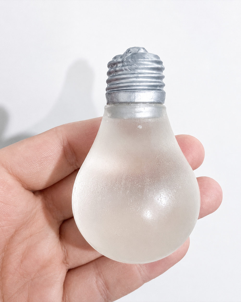 a glow-in-the-dark light bulb squishy with a frosted translucent body, metallic silver cap, soft squeezable texture, and classic bulb-inspired shape