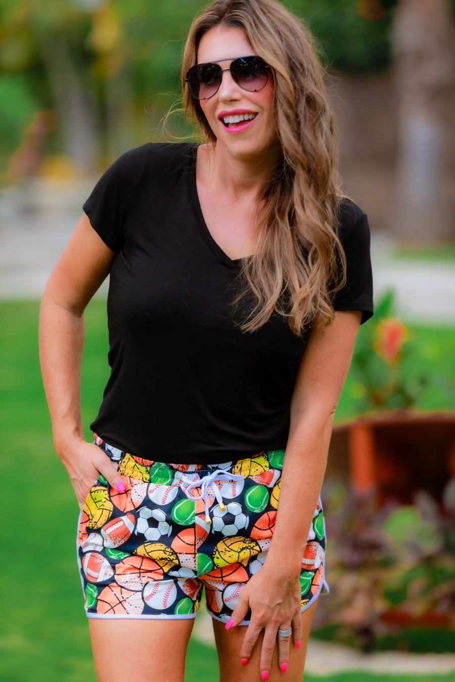 mid-rise relaxed fit activewear shorts with side pockets and a tie waist drawstring with gold bead accents, designed on a multi-sport pattern print fabric, black base, and ivory trim