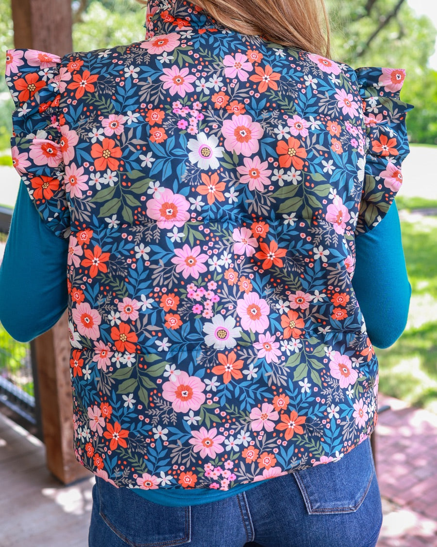 puffer vest with a collared neckline, short flutter sleeves, a button-up front, and hidden pockets on a fully lined quilted fabric in olive, orange, pink, teal, and white floral pattern
