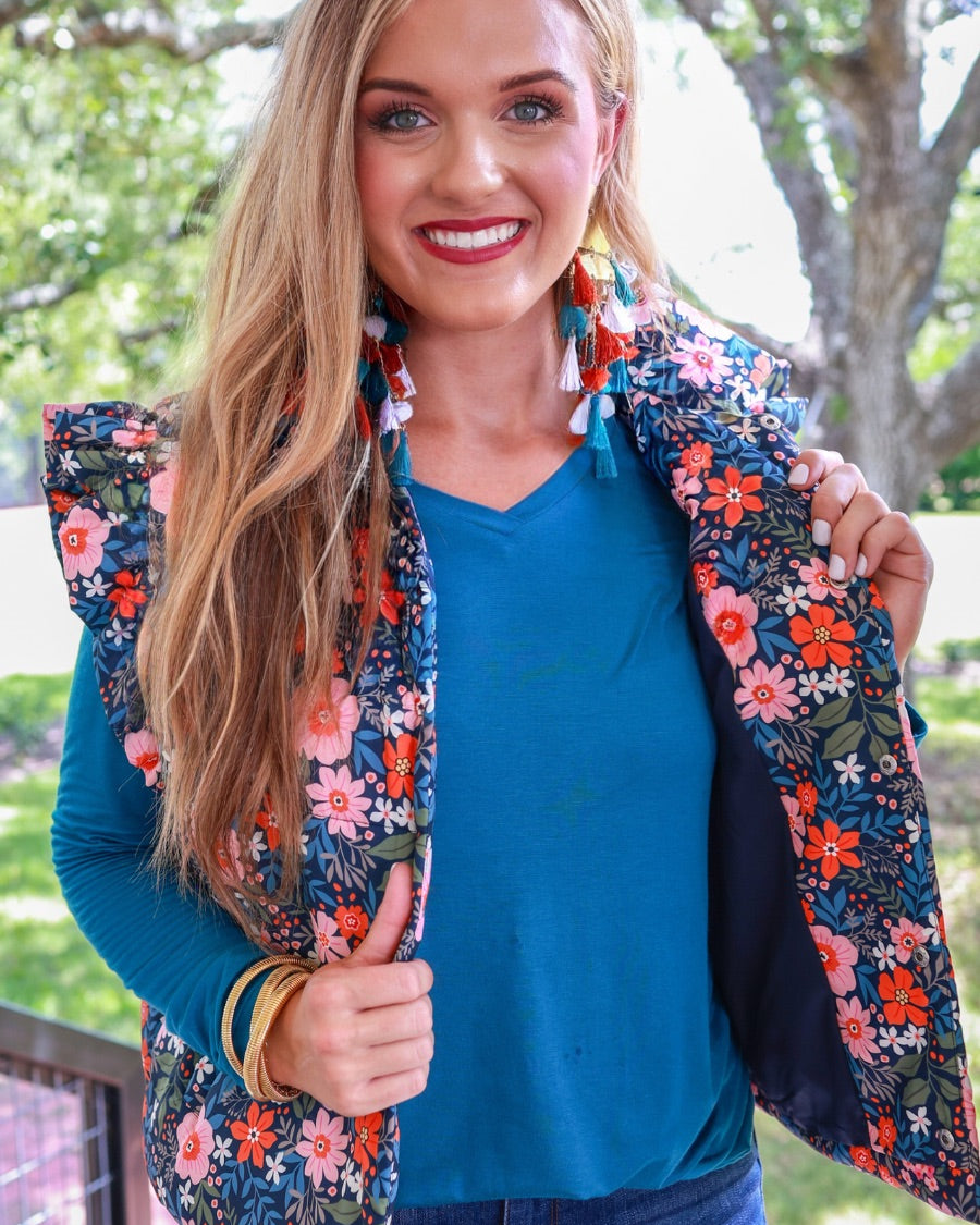 puffer vest with a collared neckline, short flutter sleeves, a button-up front, and hidden pockets on a fully lined quilted fabric in olive, orange, pink, teal, and white floral pattern