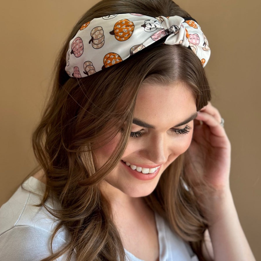 a twisted center top knot headband crafted from soft, lightweight material with a multicolor jack-o-lantern pattern on a ivory base