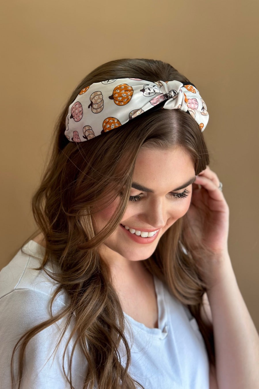 a twisted center top knot headband crafted from soft, lightweight material with a multicolor jack-o-lantern pattern on a ivory base