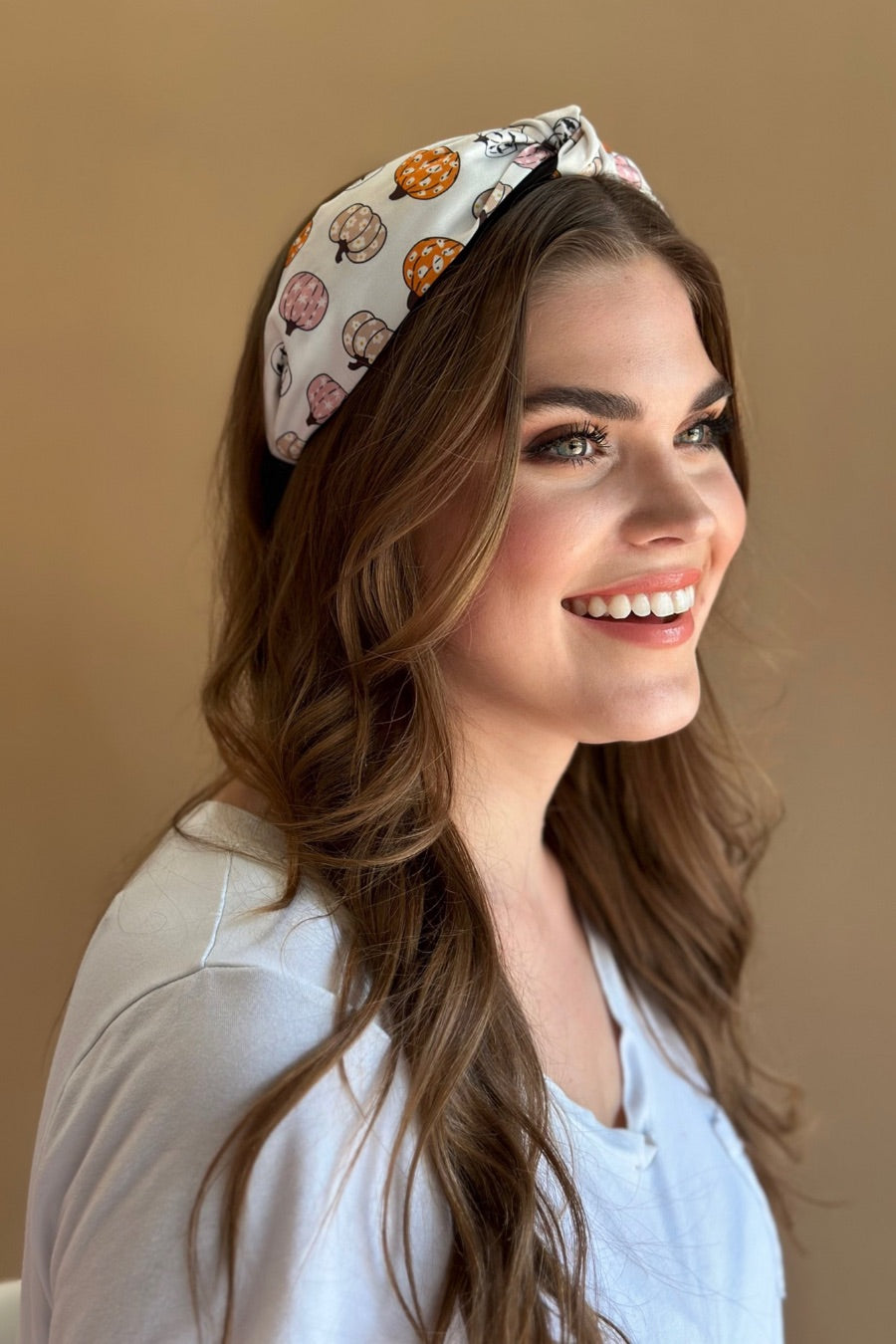 a twisted center top knot headband crafted from soft, lightweight material with a multicolor jack-o-lantern pattern on a ivory base