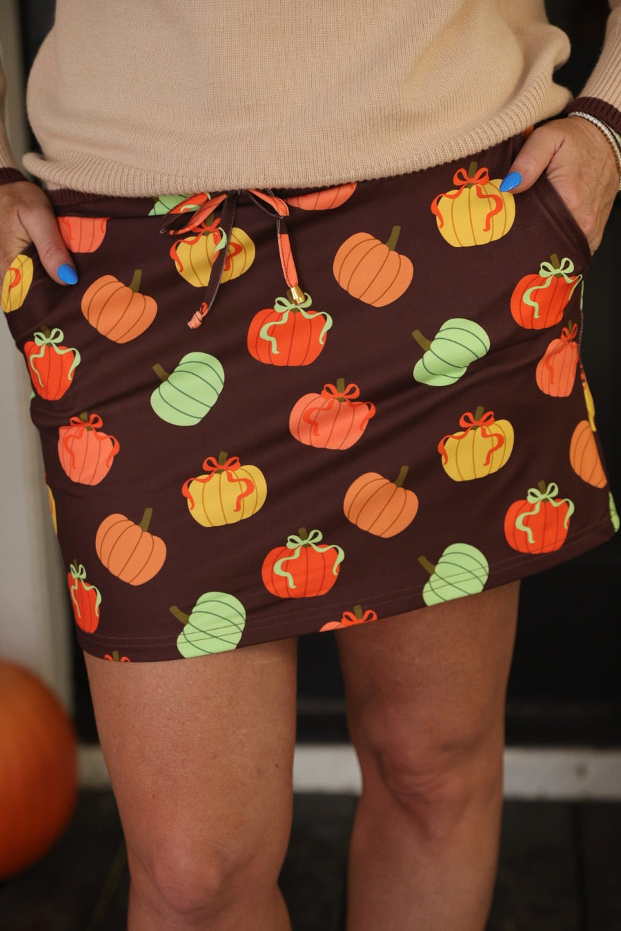 mid-rise relaxed fit everyday skort made of lightweight material with built-in brown shorts, drawstring tie with gold bead accents, an elastic band on the back, and side pockets, designed on a multicolor pumpkin print and brown base