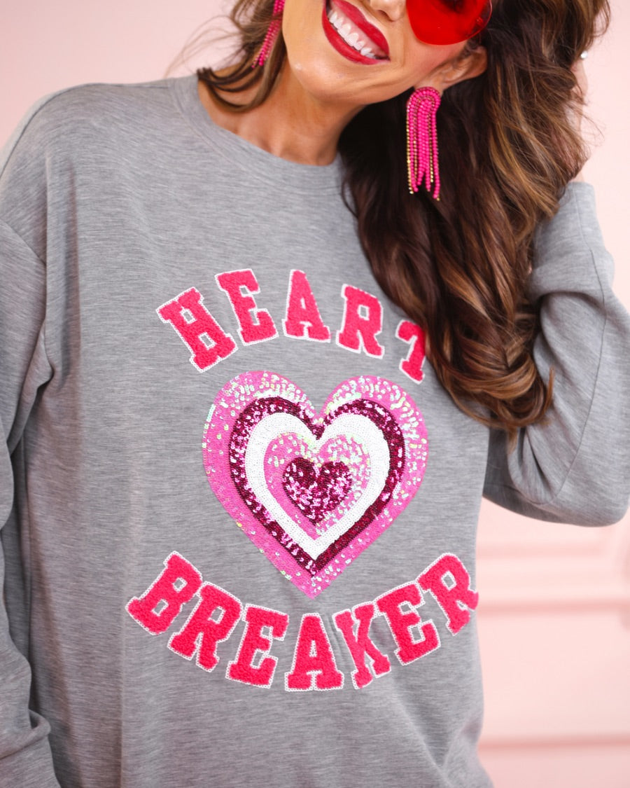 a gray long-sleeve pullover made from luxe material with chenille 'HEART BREAKER' lettering, a layered sequin heart detail, relaxed drop-shoulder fit, and ribbed neckline, cuffs, and hem for an effortlessly elevated look
