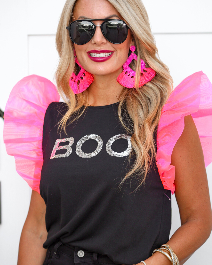 a solid black lightweight top crafted from soft fabric with shimmering silver sequin 'BOO' lettering across the front chest, neon pink organza ruffle sleeves, rounded neckline, and statement Halloween-inspired design