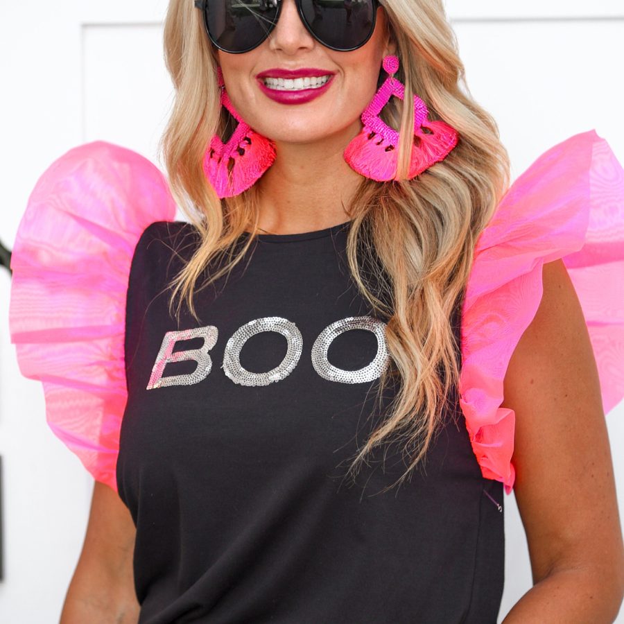 a solid black lightweight top crafted from soft fabric with shimmering silver sequin 'BOO' lettering across the front chest, neon pink organza ruffle sleeves, rounded neckline, and statement Halloween-inspired design