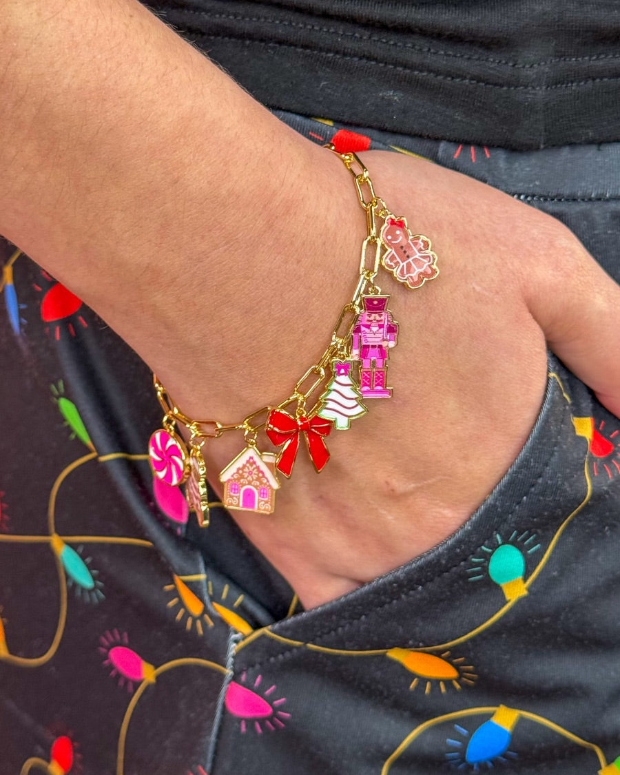an adjustable gold link bracelet adorned with whimsical enamel charms (a bold red bow, Christmas bear, Christmas tree, gingerbread girl, gingerbread house, pink nutcracker, and a pink peppermint)