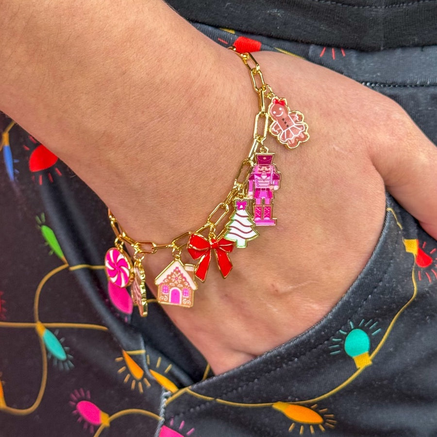 an adjustable gold link bracelet adorned with whimsical enamel charms (a bold red bow, Christmas bear, Christmas tree, gingerbread girl, gingerbread house, pink nutcracker, and a pink peppermint)