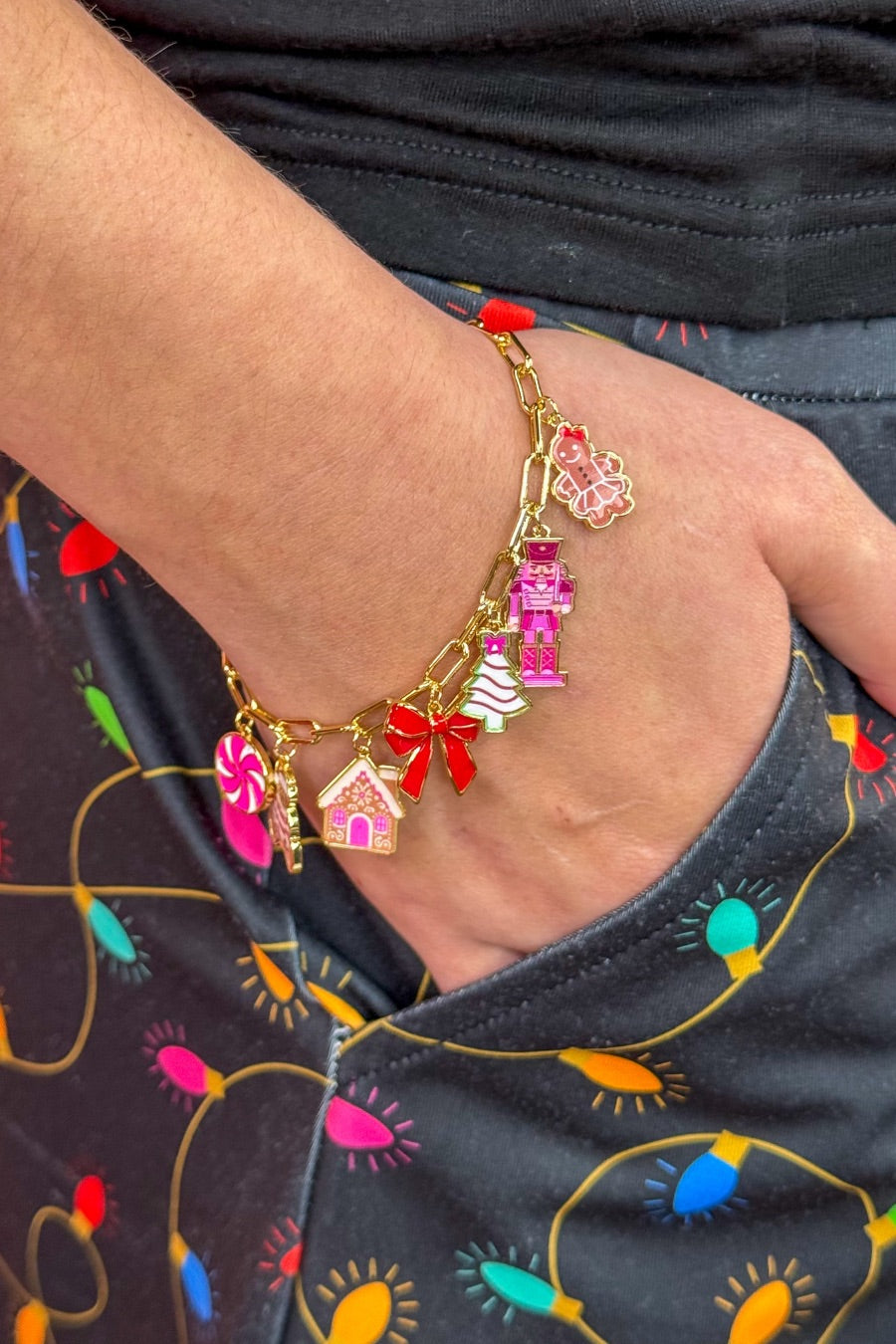 an adjustable gold link bracelet adorned with whimsical enamel charms (a bold red bow, Christmas bear, Christmas tree, gingerbread girl, gingerbread house, pink nutcracker, and a pink peppermint)