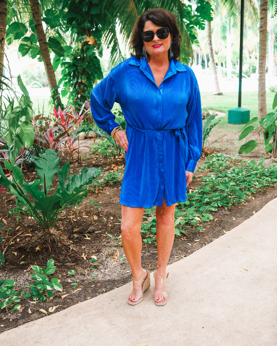 a royal blue pleated shirt dress with a classic collar, functional button front, removable waist sash, drop shoulder long sleeves, satin cuffs, back yoke seam, accordion texture, and flowy mini-length silhouette