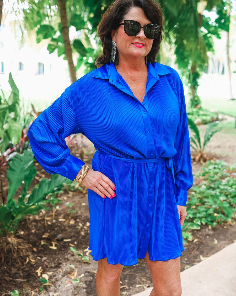 a royal blue pleated shirt dress with a classic collar, functional button front, removable waist sash, drop shoulder long sleeves, satin cuffs, back yoke seam, accordion texture, and flowy mini-length silhouette