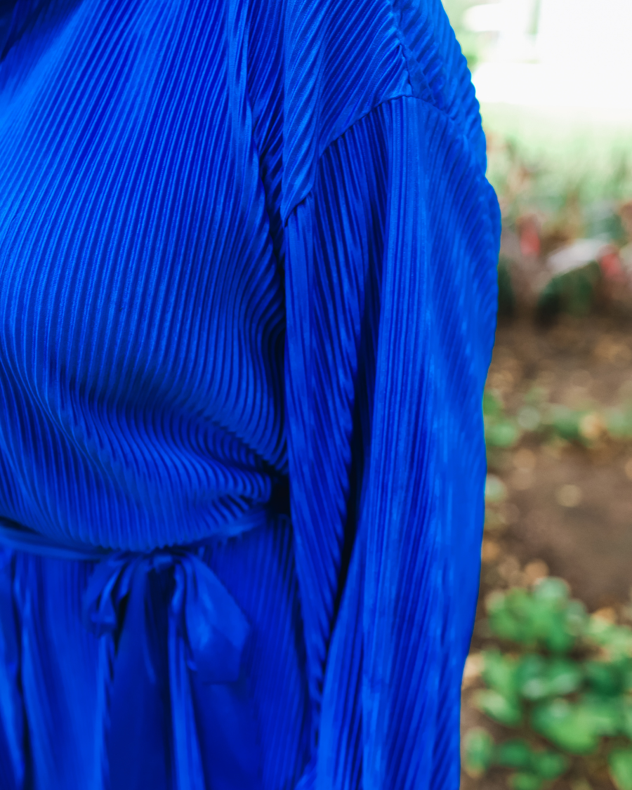 a royal blue pleated shirt dress with a classic collar, functional button front, removable waist sash, drop shoulder long sleeves, satin cuffs, back yoke seam, accordion texture, and flowy mini-length silhouette