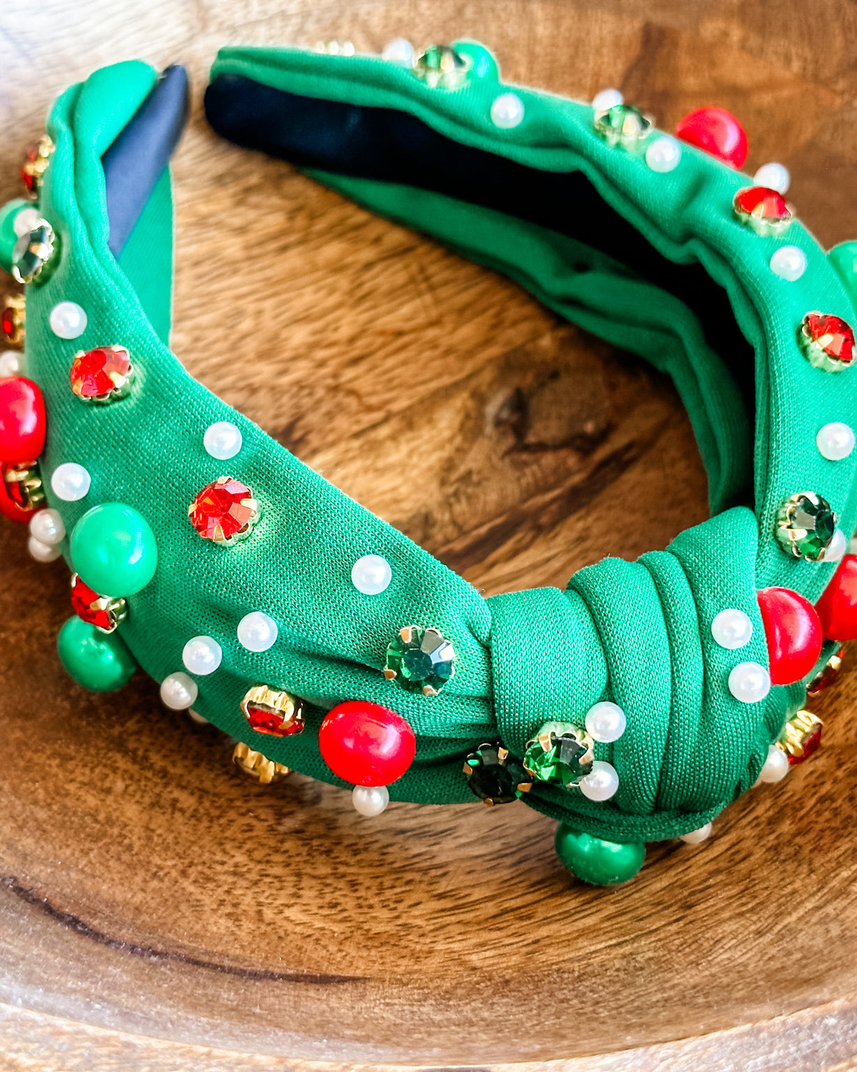 top knot adorned with jewel-tone beads, pearls, and rhinestones on velvet in green
