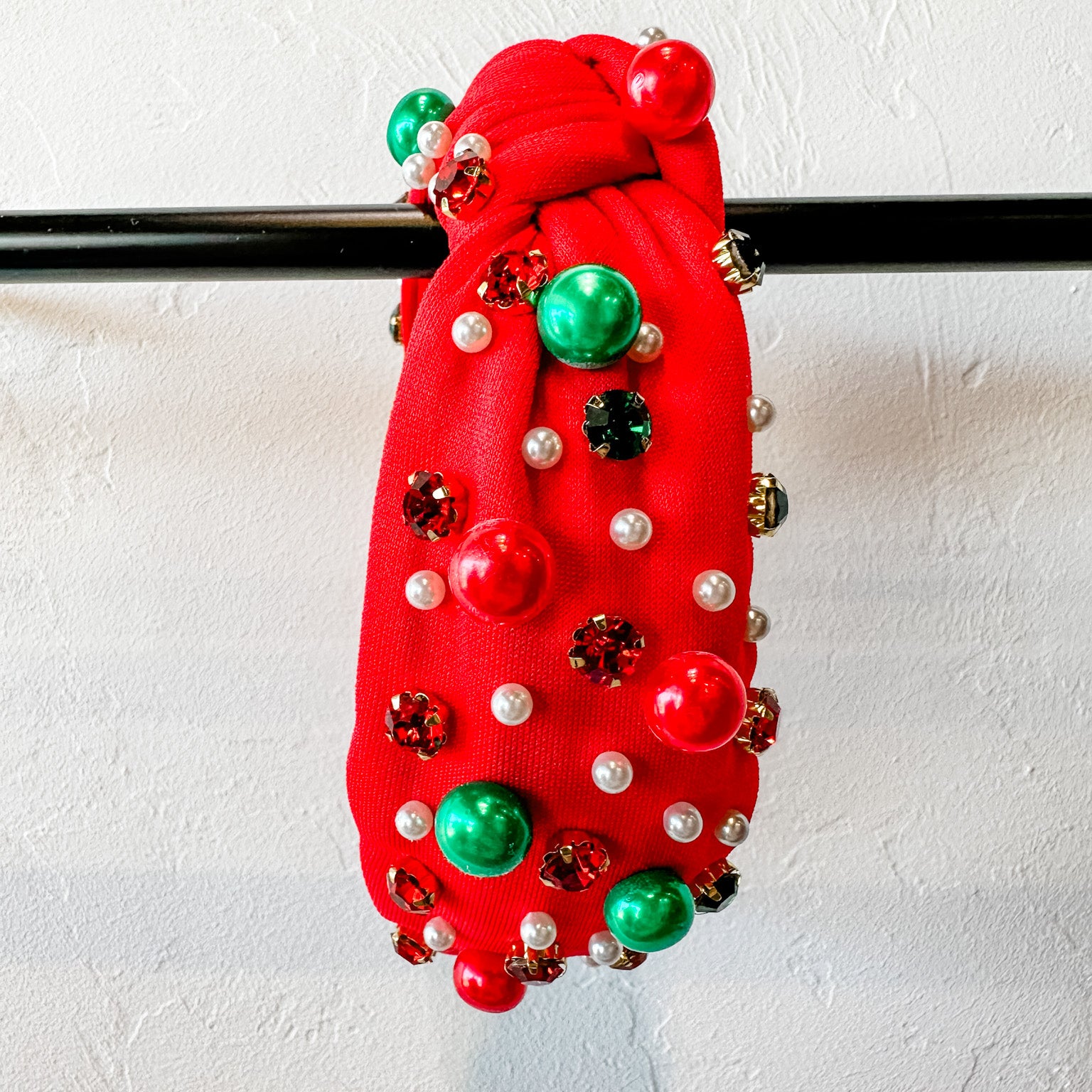 top knot adorned with jewel-tone beads, pearls, and rhinestones on velvet in red