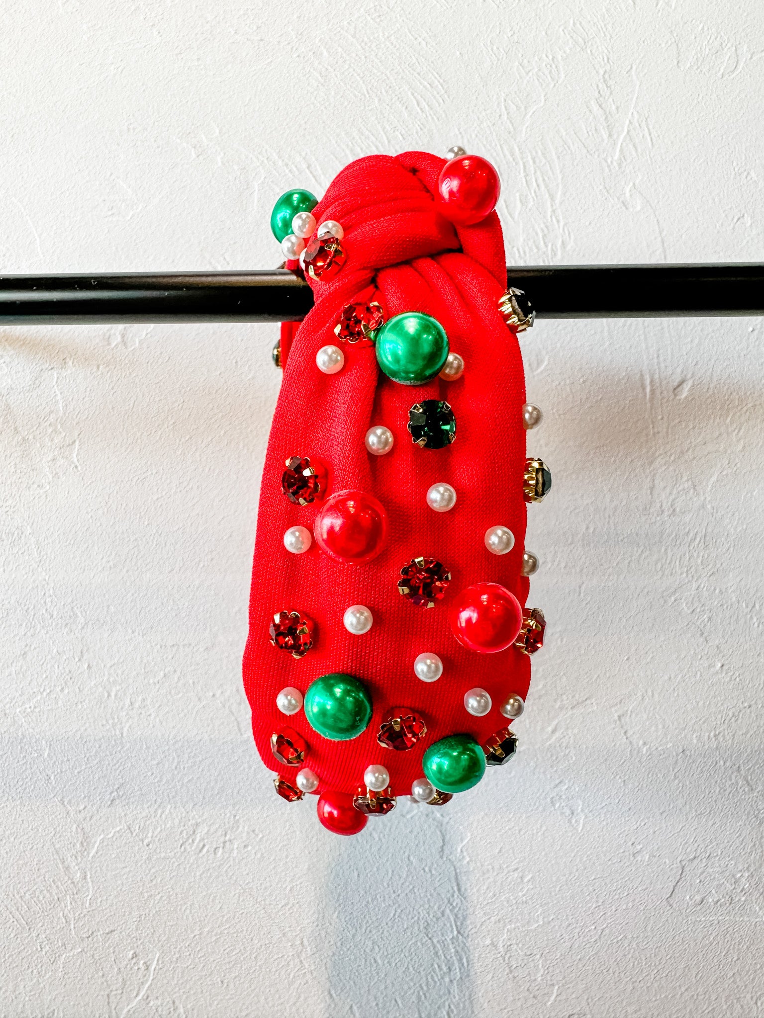 top knot adorned with jewel-tone beads, pearls, and rhinestones on velvet in red