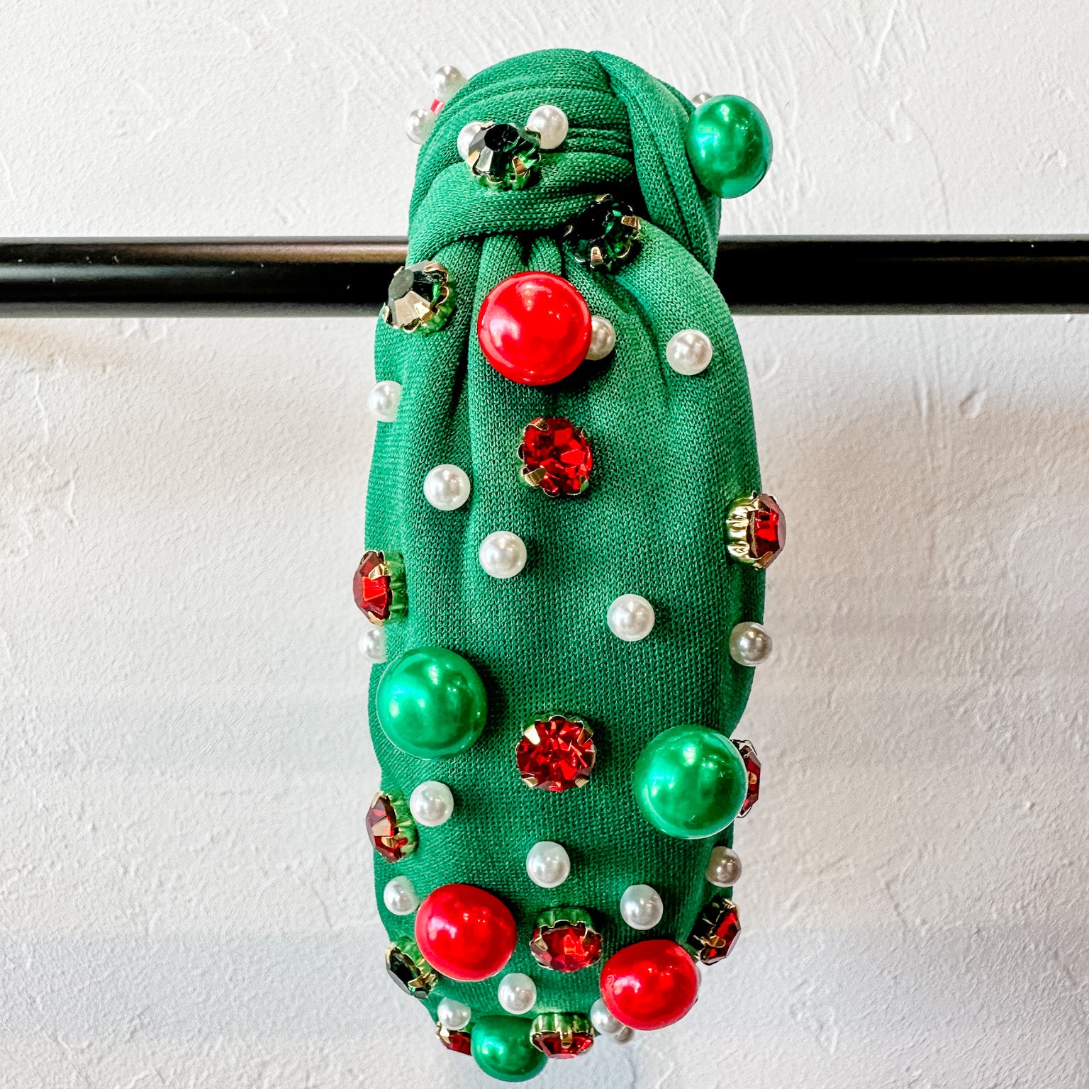 top knot adorned with jewel-tone beads, pearls, and rhinestones on velvet in green