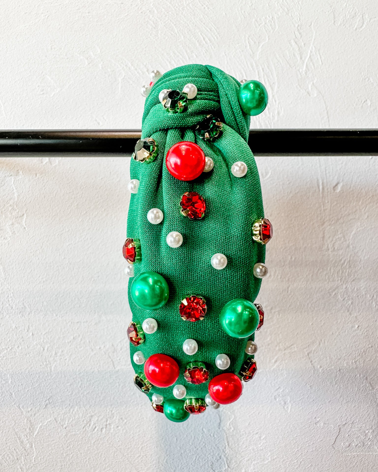 top knot adorned with jewel-tone beads, pearls, and rhinestones on velvet in green