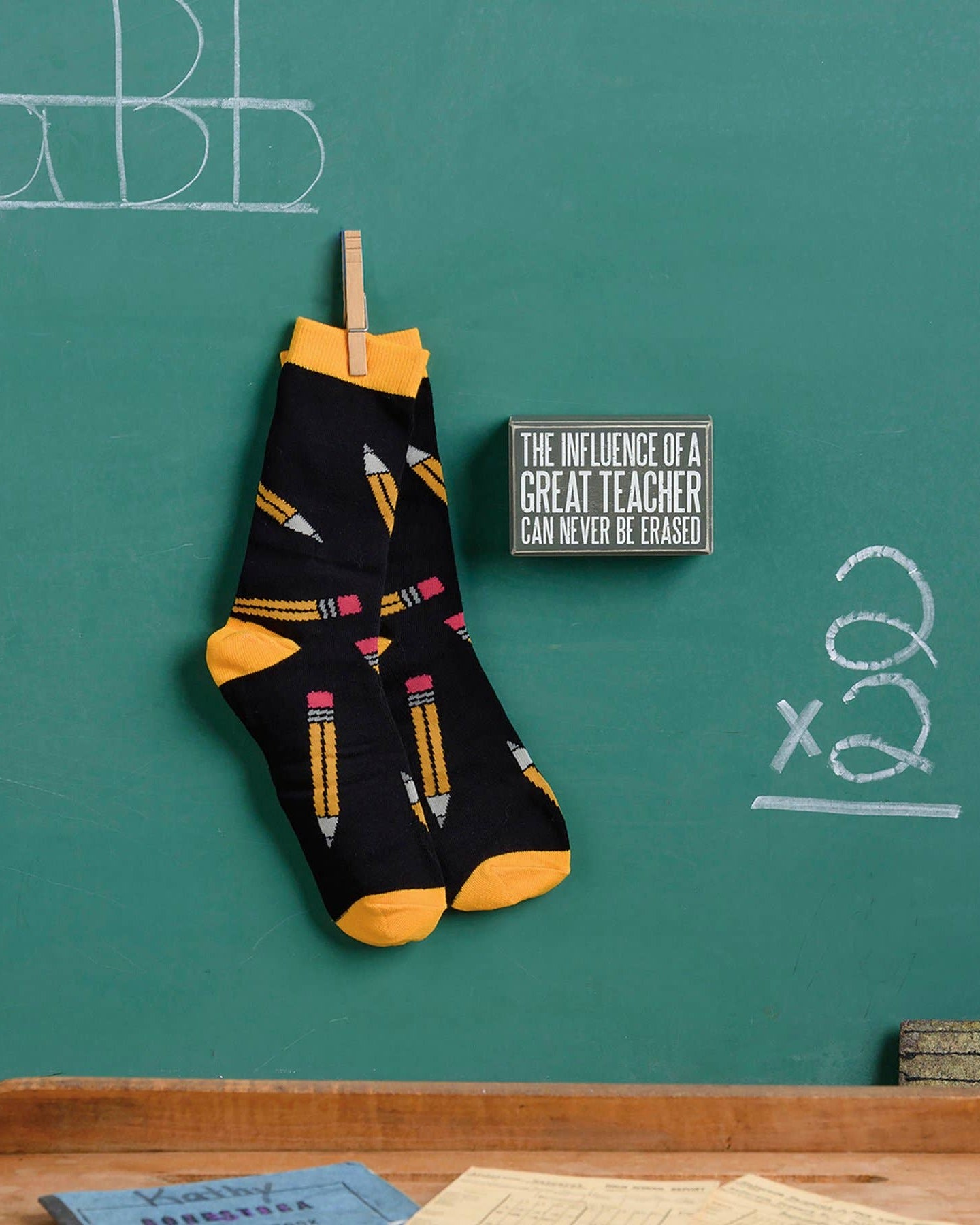Black socks with yellow accents hanging on a chalkboard with educational drawings.
