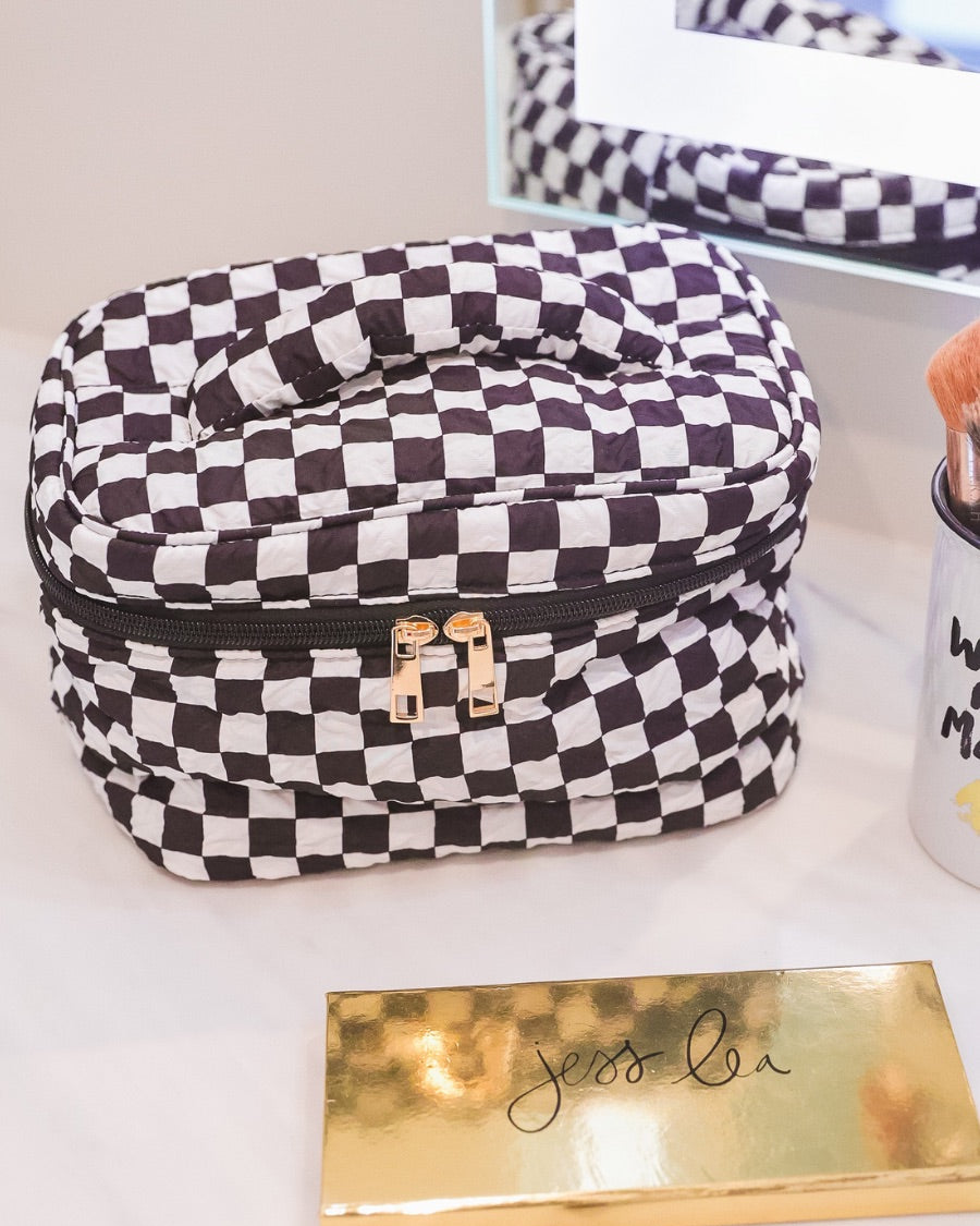 a structured bag with a spacious interior, a secure double zip around closure, a top handle, and gold accents on a quilted body in checkerboard checkered (black/white)