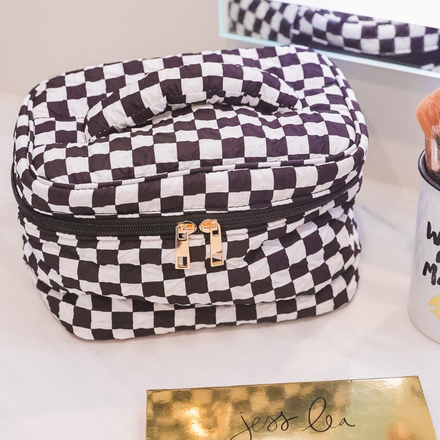 a structured bag with a spacious interior, a secure double zip around closure, a top handle, and gold accents on a quilted body in checkerboard checkered (black/white)