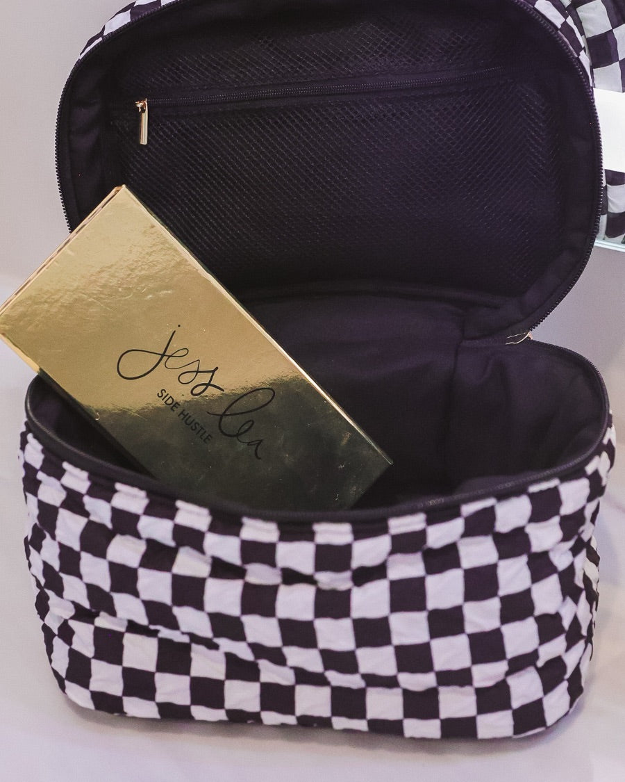 a structured bag with a spacious interior, a secure double zip around closure, a top handle, and gold accents on a quilted body in checkerboard checkered (black/white)