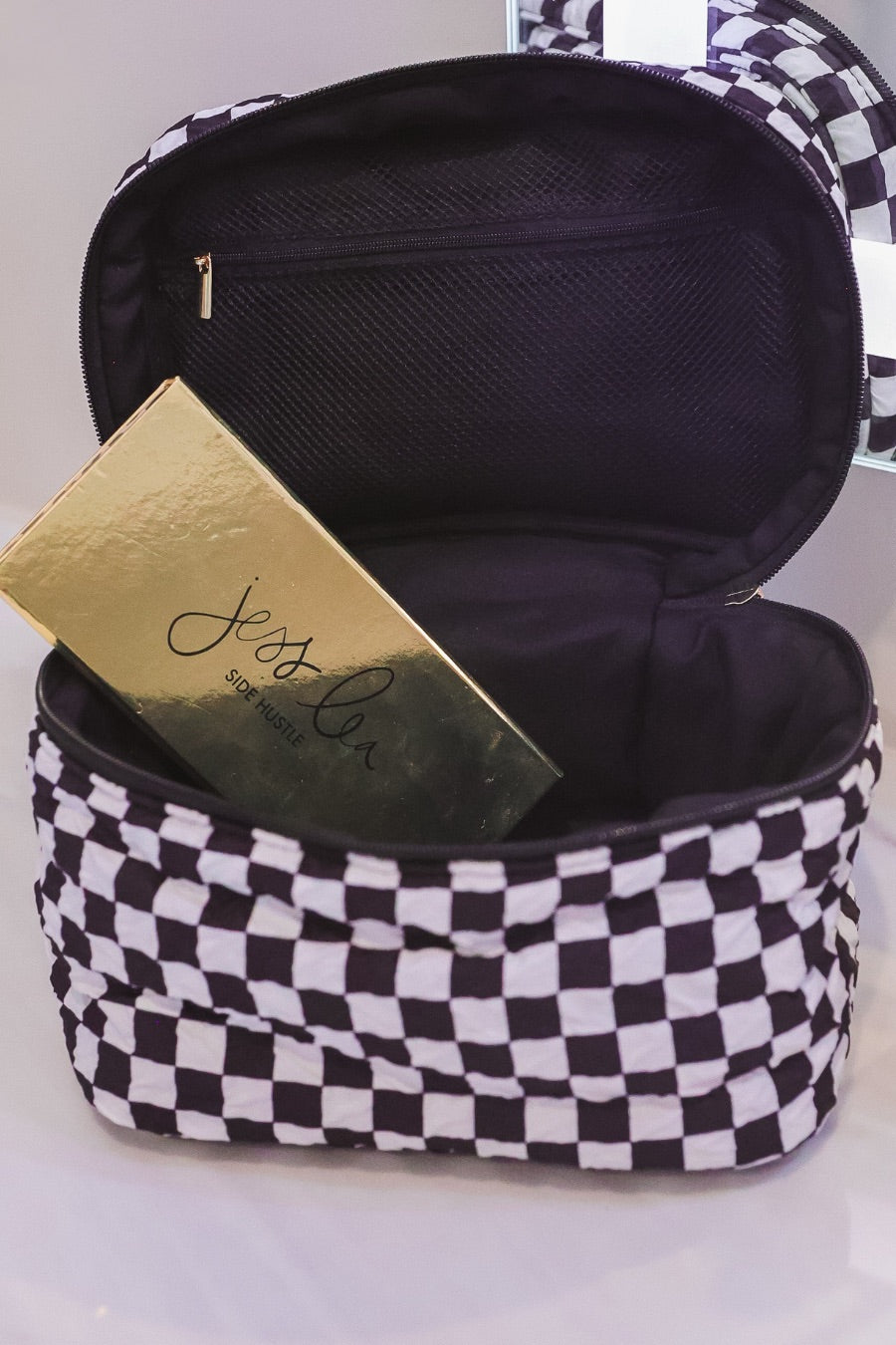 a structured bag with a spacious interior, a secure double zip around closure, a top handle, and gold accents on a quilted body in checkerboard checkered (black/white)