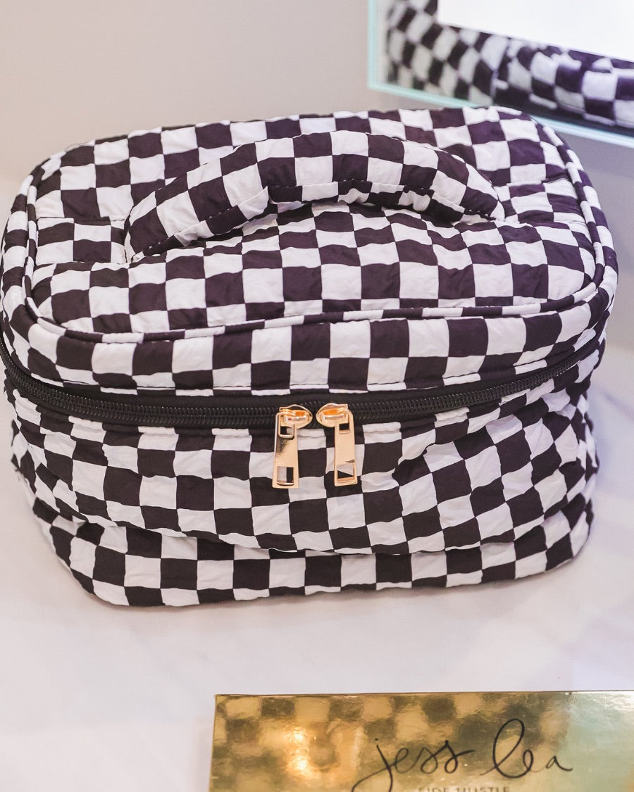 a structured bag with a spacious interior, a secure double zip around closure, a top handle, and gold accents on a quilted body in checkerboard checkered (black/white)
