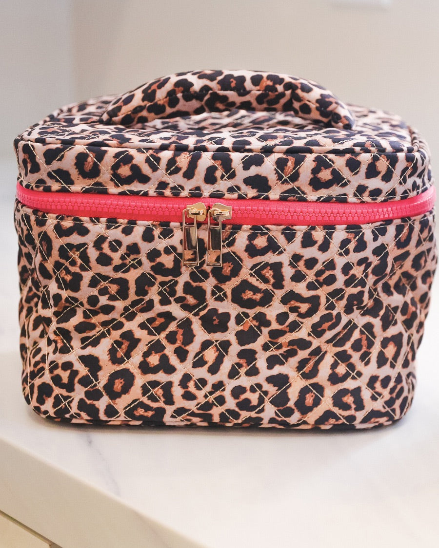 a structured bag with a spacious interior, a secure double zip around closure, a top handle, and gold accents on a quilted body in safari chic (leopard)