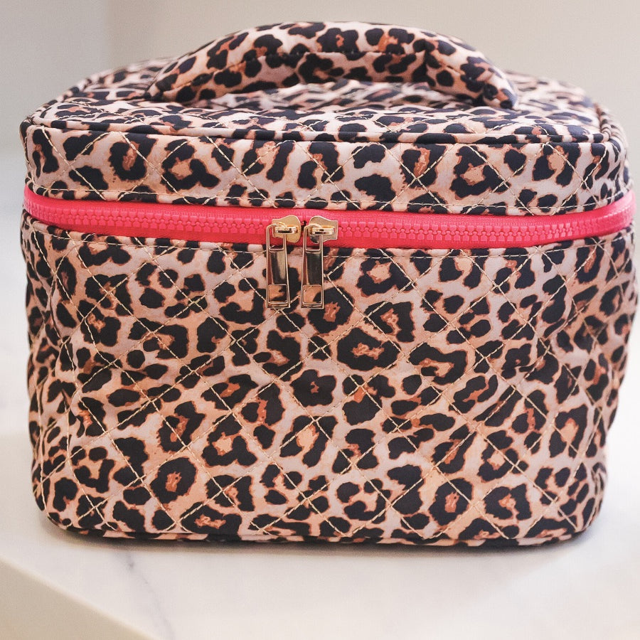 a structured bag with a spacious interior, a secure double zip around closure, a top handle, and gold accents on a quilted body in safari chic (leopard)