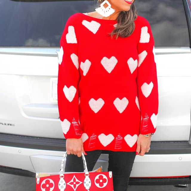 a long-sleeve sweater with an allover white heart motif, distressed cuffs, and a worn hem finish