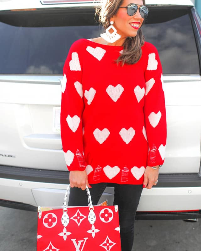 a long-sleeve sweater with an allover white heart motif, distressed cuffs, and a worn hem finish