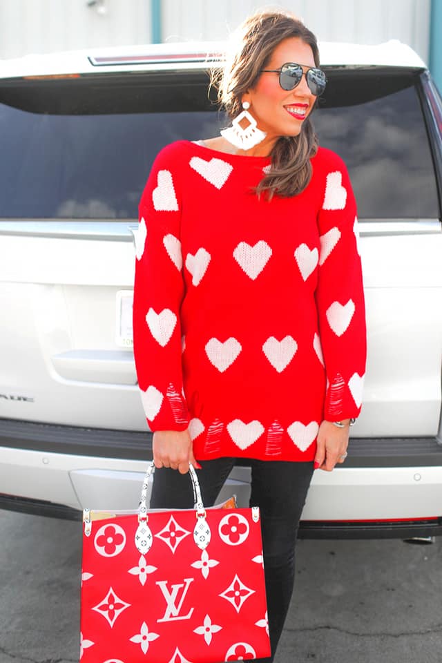 a long-sleeve sweater with an allover white heart motif, distressed cuffs, and a worn hem finish
