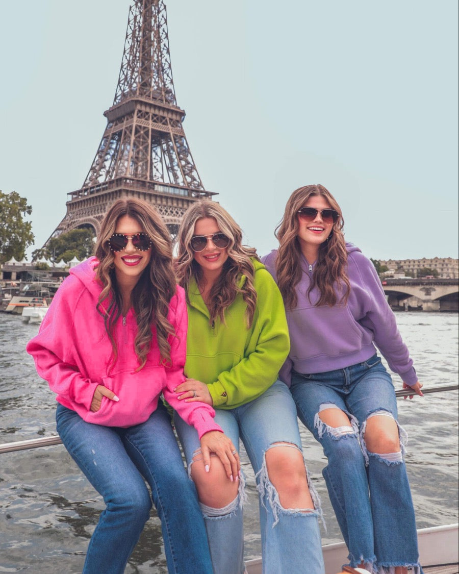 a cropped hooded quarter zip pullover with a relaxed fit, functional kangaroo pocket, and thumb holes in pink, neon lime, and lavender