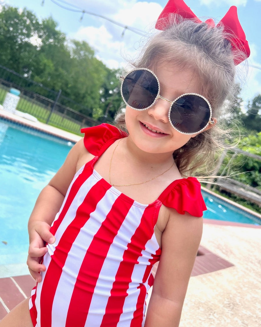 kids' sunglasses with rose gold frame and bridge, black round lenses, rhinestone trim, black temple tips featuring the brand name in white, nose pads, UV protection, and a signature pouch