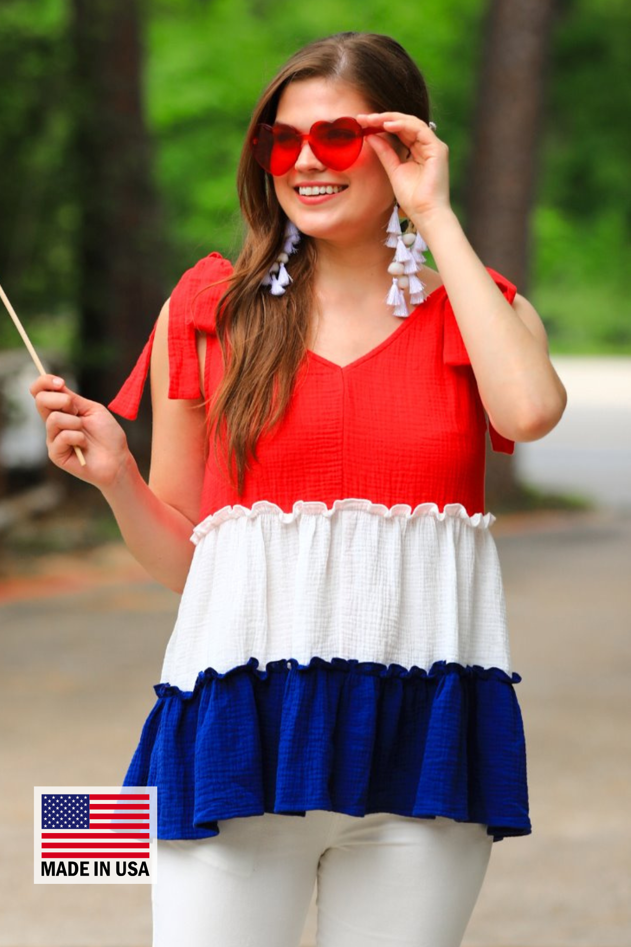 a red tiered color block top with a V-neckline front and back, adjustable wide tie straps, a ruffled hem, and a relaxed, lightweight fit, accented with a MADE IN USA watermark in the bottom left-hand corner